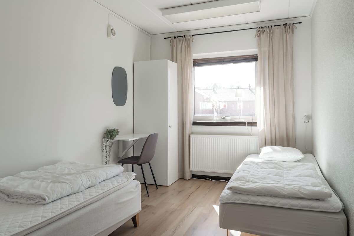 A modern, well-lit bedroom with two beds, a desk, and a radiator.