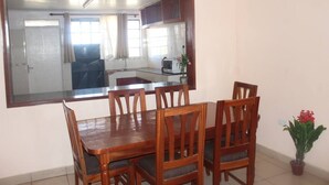 A dining area with a wooden table and chairs, a large mirror, and a view into the kitchen.