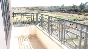 A balcony with a metal railing overlooking a sports field and a parked yellow vehicle.