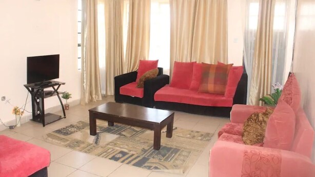 A living room with two sofas, a coffee table, a TV on a stand, and a window with curtains.