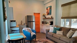 A compact living space with a dining area, a sofa, a kitchen, and a window with a view. - Studio - direct 2 min beach walk with public access end of street. (Oak Island)