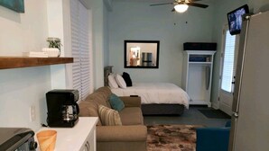 A compact hotel room with a kitchenette, a sofa, a bed, and a television. - Studio - direct 2 min beach walk with public access end of street. (Oak Island)