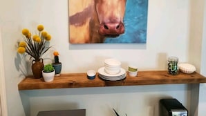 A painting of a cow on a wall above a wooden shelf with decorative items. - Studio - direct 2 min beach walk with public access end of street. (Oak Island)