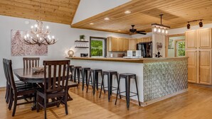 A modern kitchen with wooden ceiling beams, a central island with stools, and a dining area with a round table and chairs.