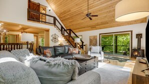 A spacious living room with a high ceiling, a staircase, a fireplace, and large windows.