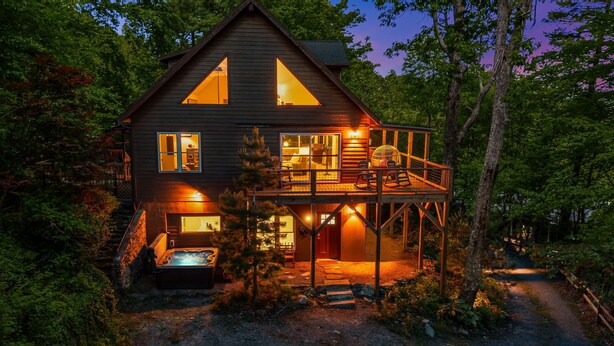 A two-story cabin with a hot tub, a deck, and a large window.
