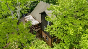 A two-story house with a balcony, surrounded by dense green foliage.