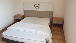 Una cama bien hecha con un diseño de corazón en la cabecera, dos mesitas de noche y un cajón pequeño.