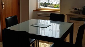 Un comedor con mesa y sillas, una ventana con cortinas, vistas al exterior y una puerta.