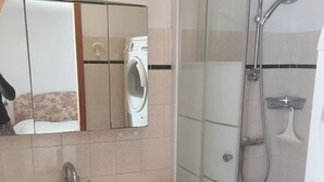 Un baño con lavamanos blanco, espejo, ducha con cerramiento de vidrio y lavadora.