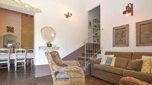 A living room with a brown sofa, wicker chairs, a dining table with chairs, a staircase, and a wall-mounted mirror. - Amazing home in Chiaramonte Gulfi RG (Chiaramonte Gulfi RG)