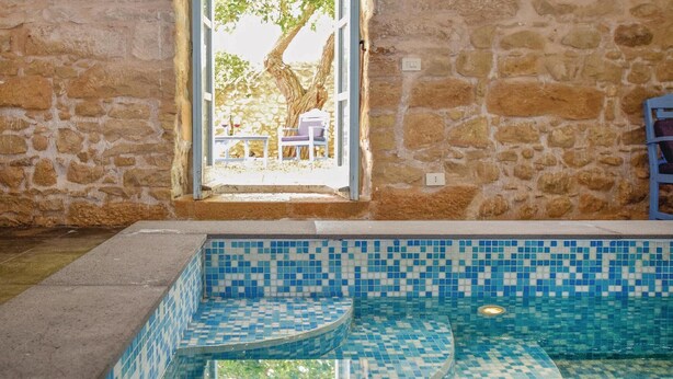 A stone-walled indoor pool with blue mosaic tiles and a view of an outdoor seating area through a window. - Amazing home in Chiaramonte Gulfi RG (Chiaramonte Gulfi RG)