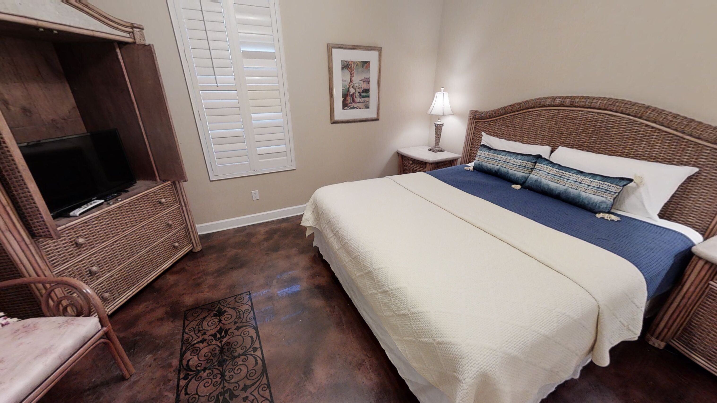 A bedroom with a large bed, a television in a wooden cabinet, a nightstand with a lamp, and a framed picture on the wall.