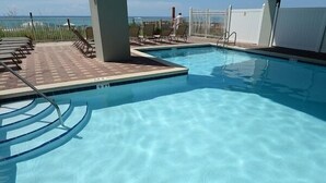 En swimmingpool med kristallklart blått vatten, omgiven av solstolar och ett vitt staket.
