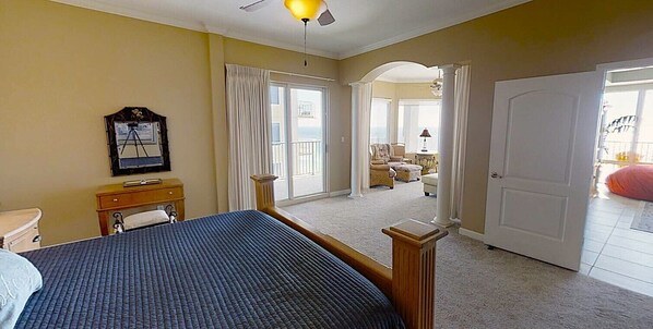 A bedroom with a bed, a desk, a chair, a window, and a door leading to another room.