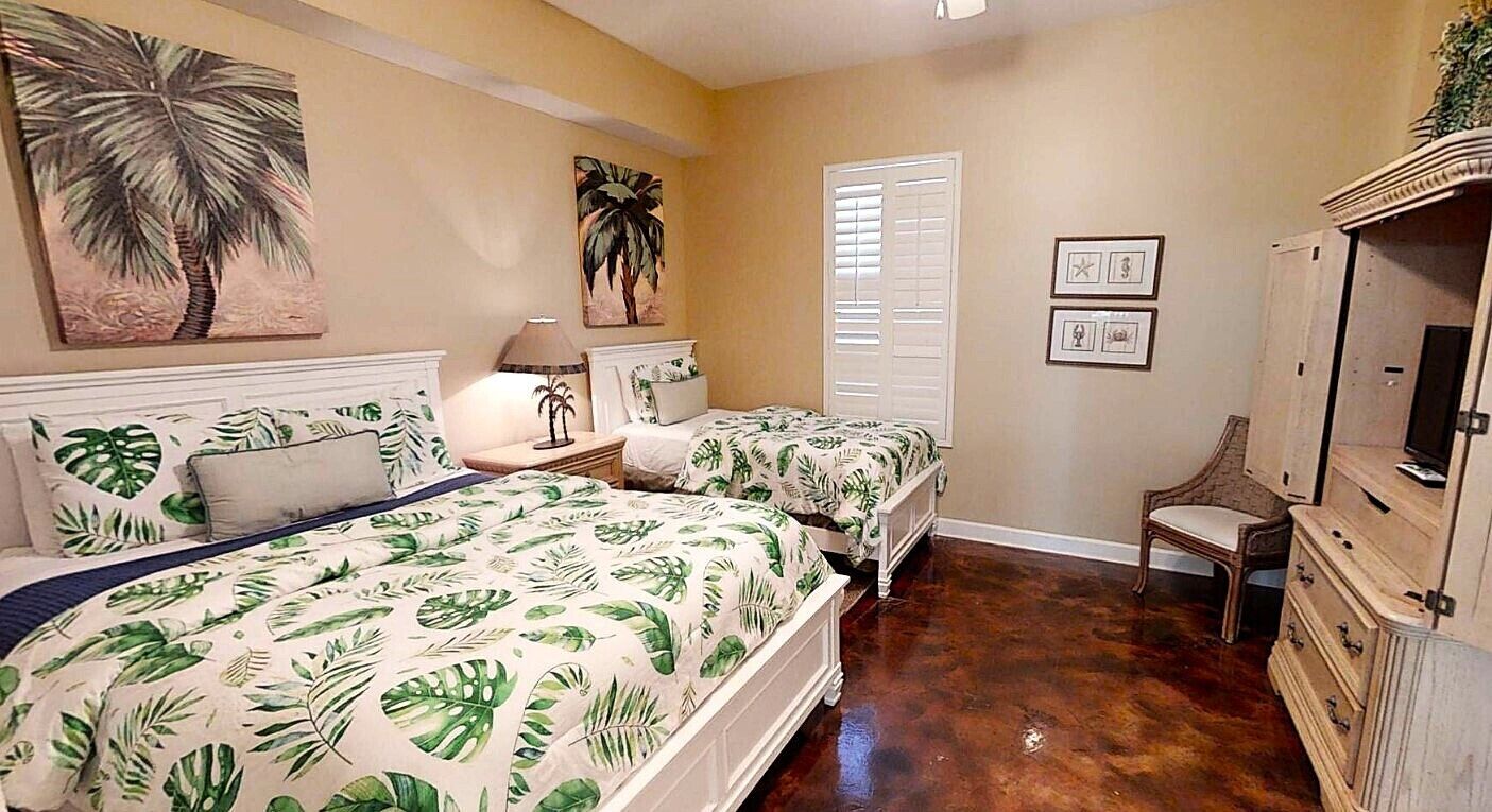Een slaapkamer met twee bedden, een nachtkastje, een lamp, een stoel en een televisie op een houten kast.