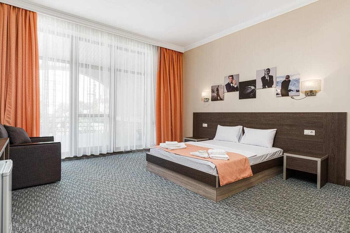 Habitación de hotel con una cama grande, un escritorio y una silla. Hay cortinas, una lámpara de pared y un cuadro en la pared.