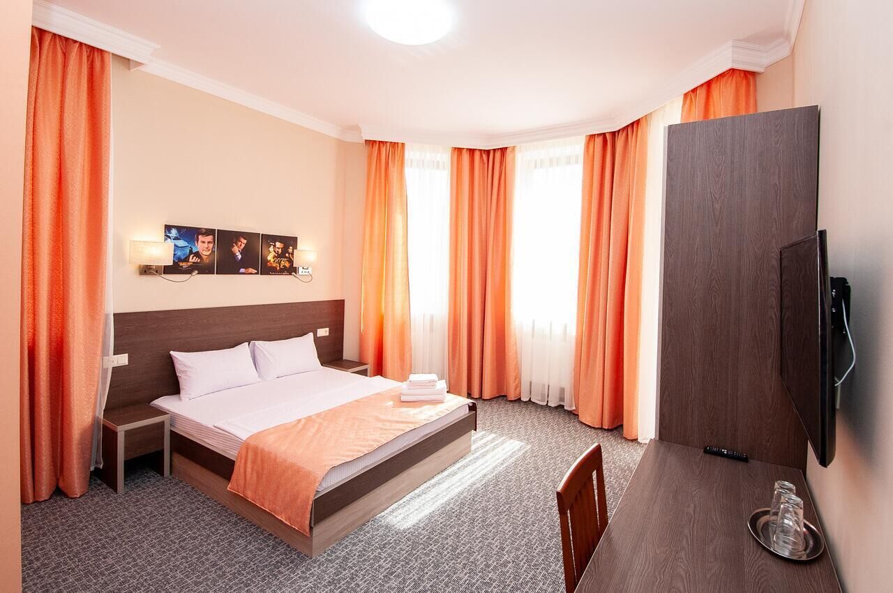 Ein Hotelzimmer mit einem großen Bett, einem flachbildfernseher an der Wand, einem kleinen Tischchen mit Tablett und einem Sessel.
