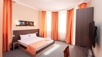 Ein Hotelzimmer mit einem großen Bett, einem flachbildfernseher an der Wand, einem kleinen Tischchen mit Tablett und einem Sessel.