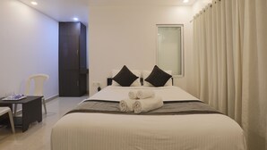 A hotel room with a bed, two pillows, a bedside table, a chair, and a window with curtains. - Aaria Hills (Arambol)