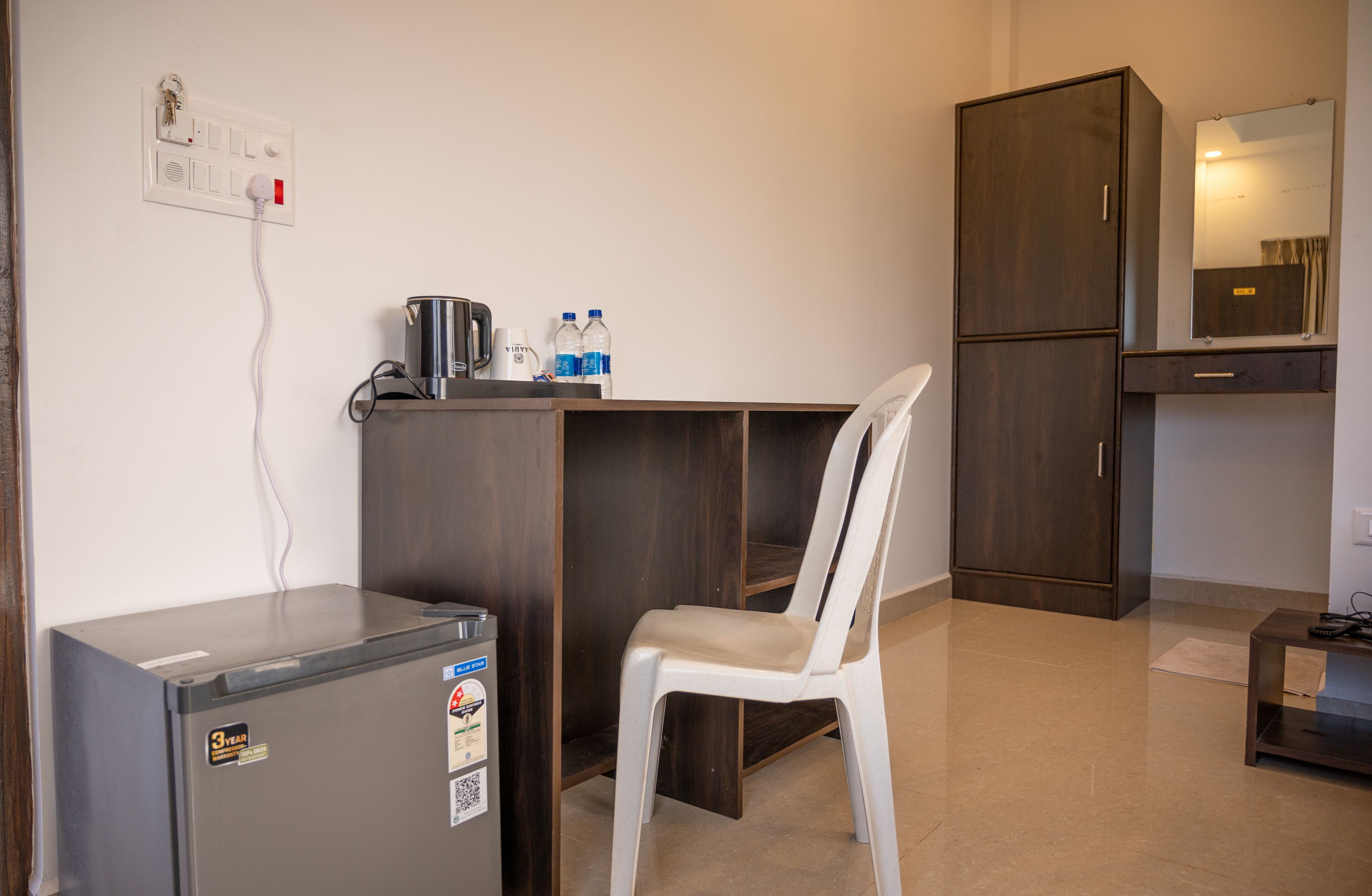 A compact room with a kitchenette, a small refrigerator, a chair, a cabinet, and a mirror.