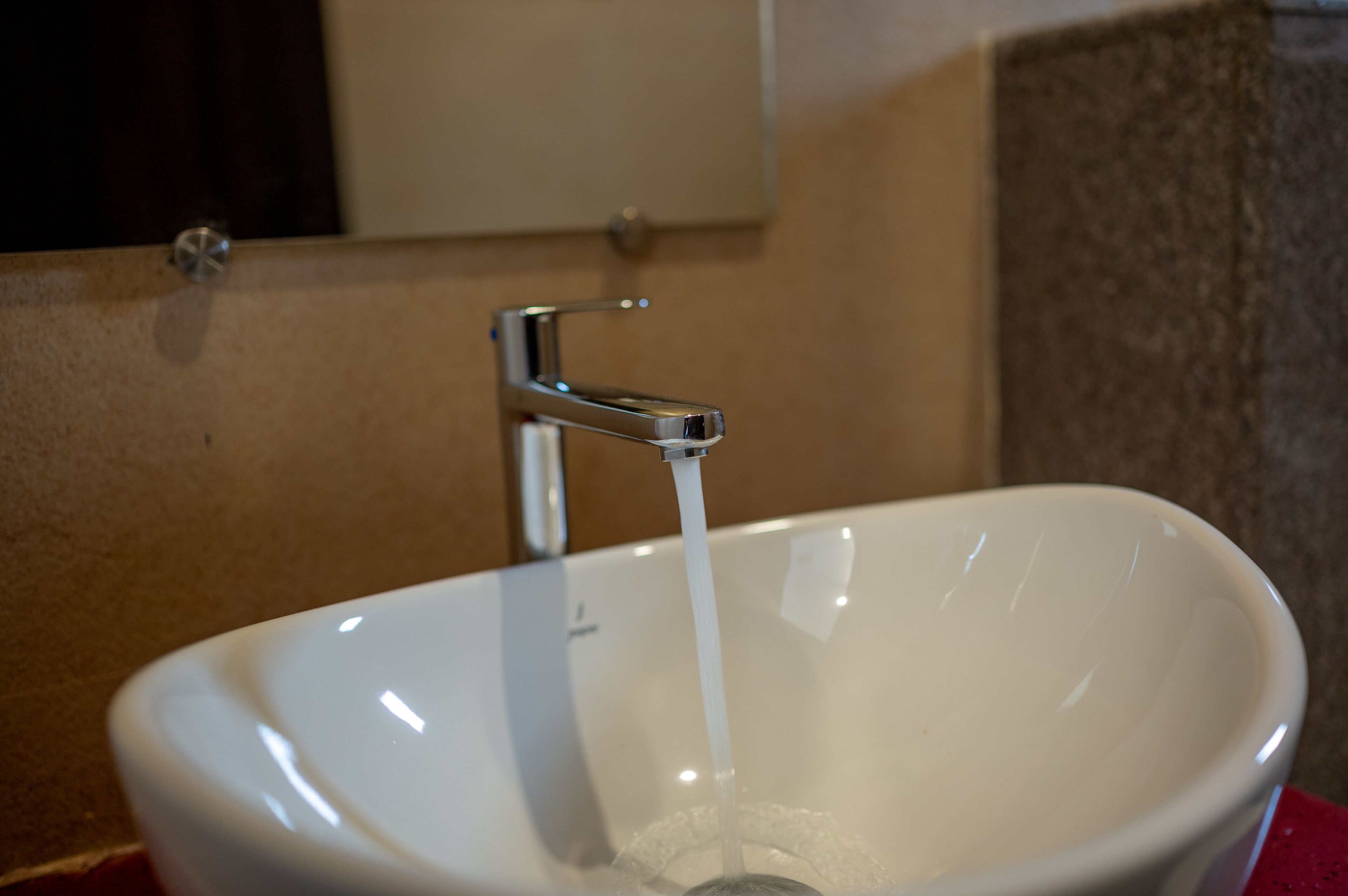 A white ceramic sink with running water, a chrome faucet, and a mirror above it.