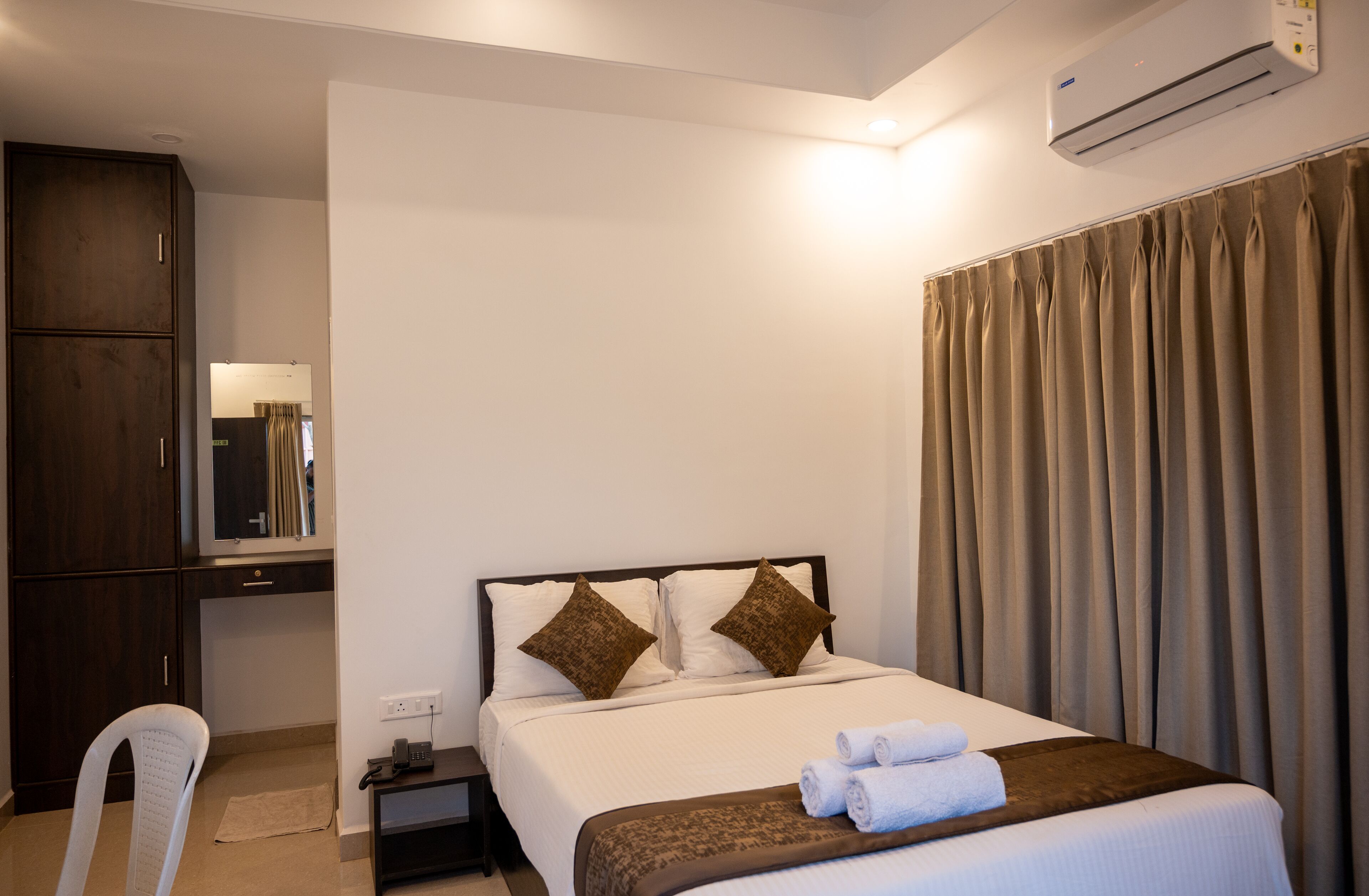 Habitación de hotel con cama, escritorio, silla, armario y aire acondicionado.