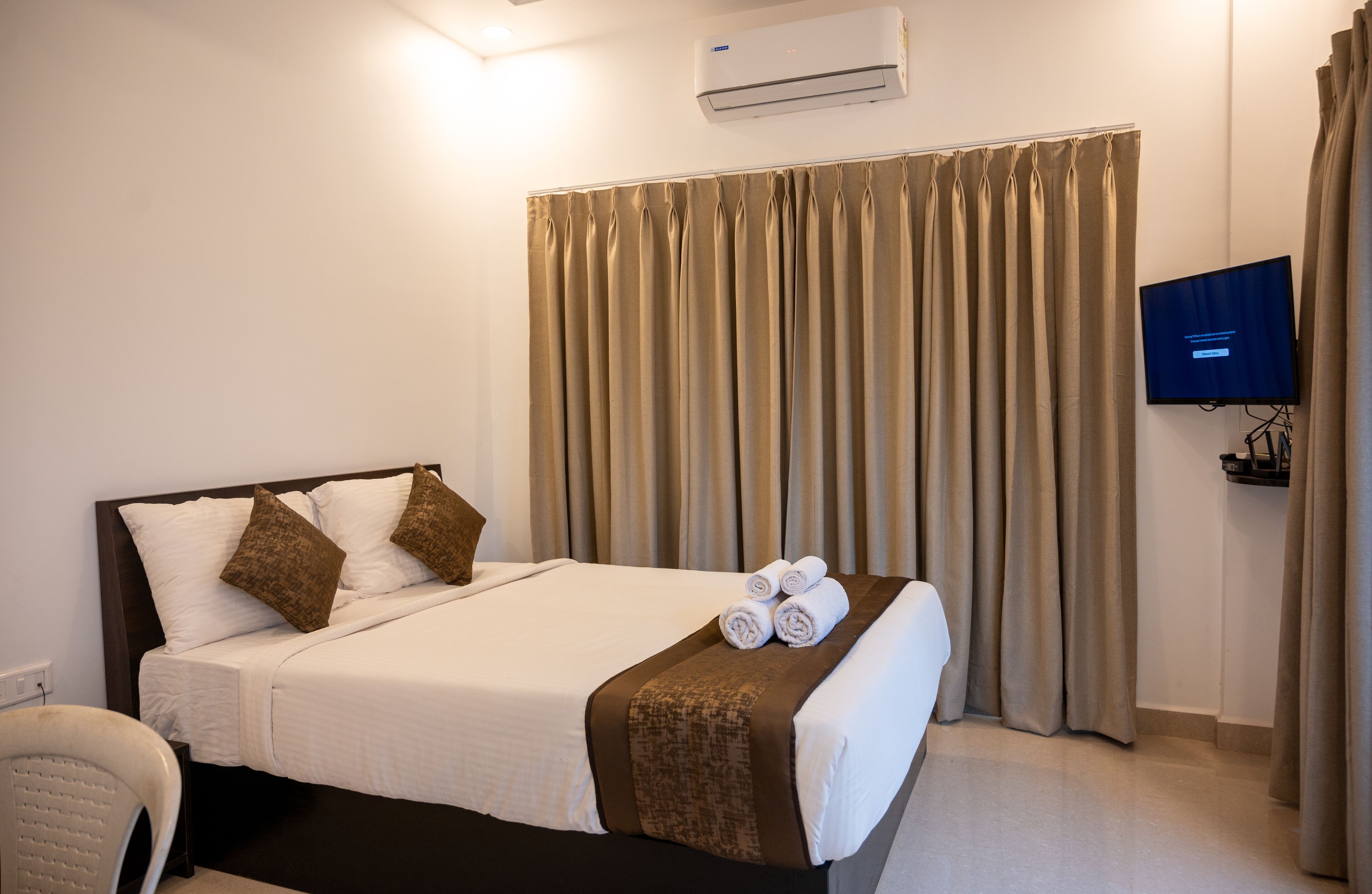 A hotel room with a bed, curtains, a TV, and an air conditioning unit.