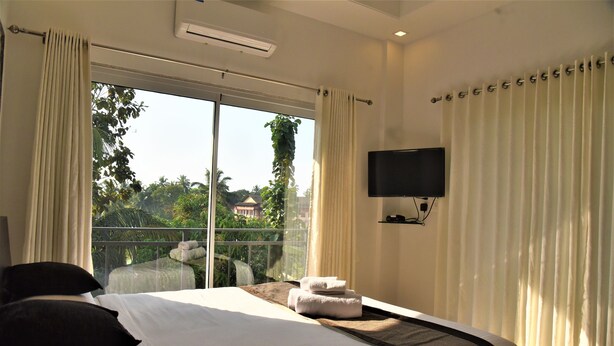 A hotel room with a large bed, a flat-screen TV mounted on the wall, and a balcony with curtains. - Aaria Hills (Arambol)