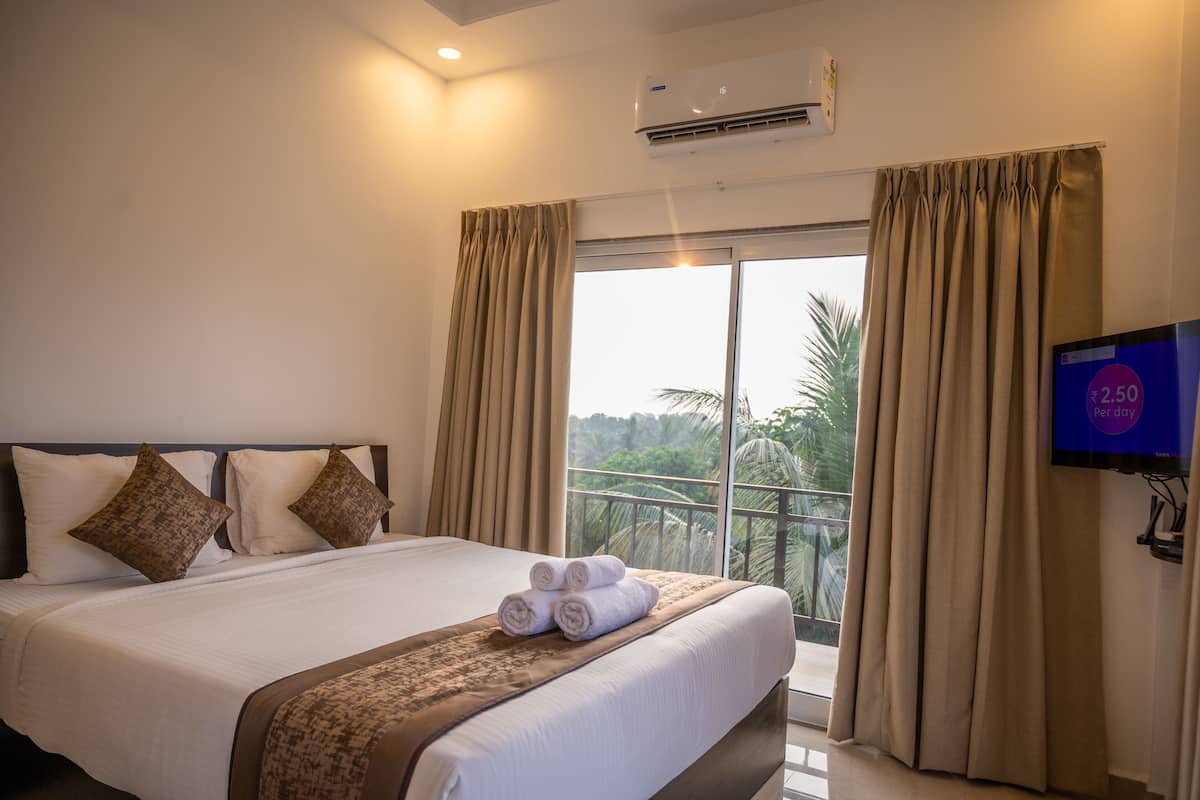 A hotel room with a large bed, beige curtains, a flat-screen TV, and a view of palm trees.