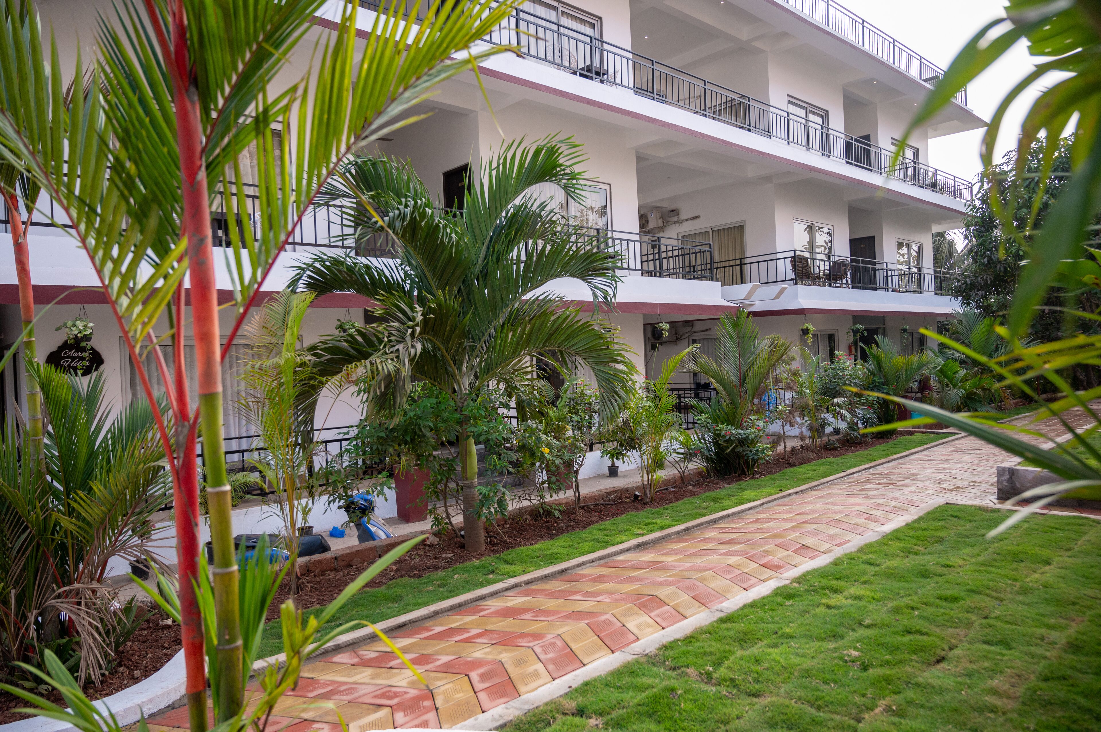 Un hotel a più piani con un cortile centrale, circondato da vegetazione lussureggiante e un vialetto lastricato.