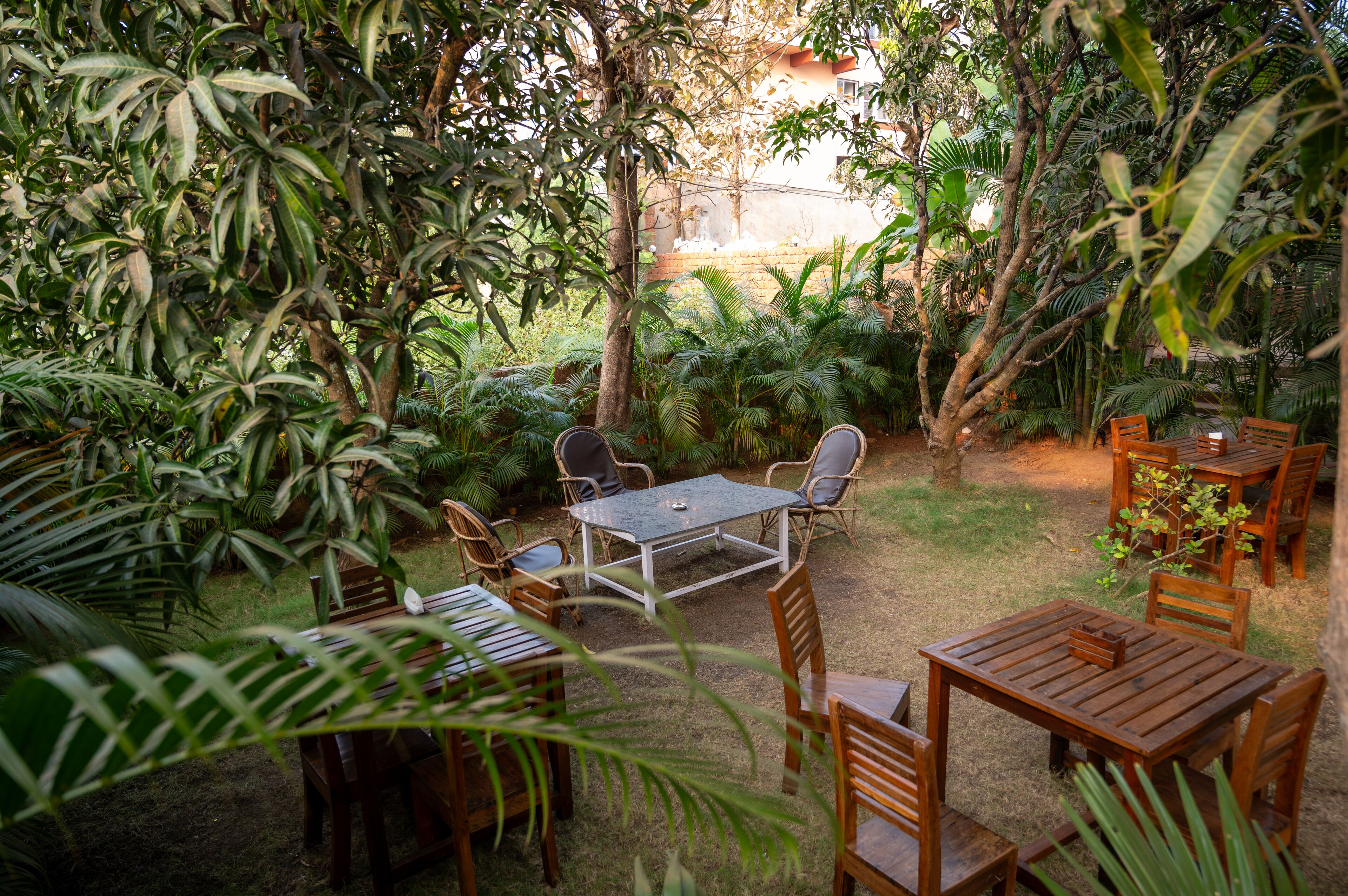 An outdoor patio with wooden tables and chairs, surrounded by lush greenery and trees.