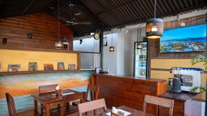 A restaurant with wooden furniture, a counter, and a large TV screen displaying a cityscape. - Aaria Hills (Arambol)
