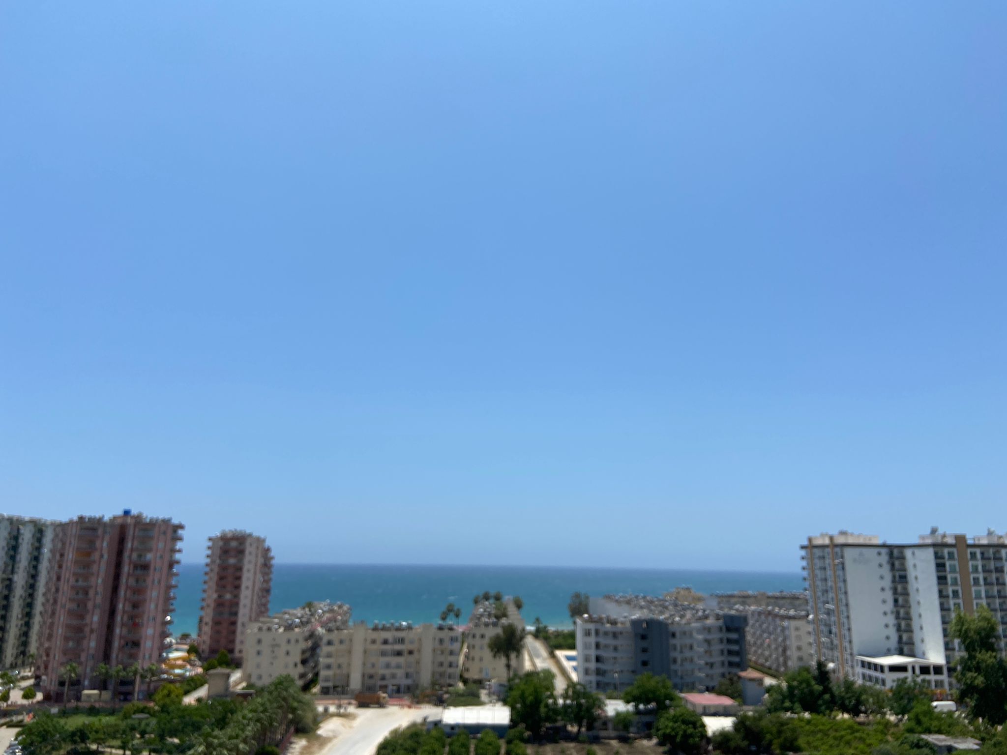 A coastal cityscape with high-rise buildings, a clear sky, and a view of the sea.