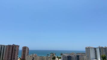 A coastal cityscape with high-rise buildings, a clear sky, and a view of the sea.