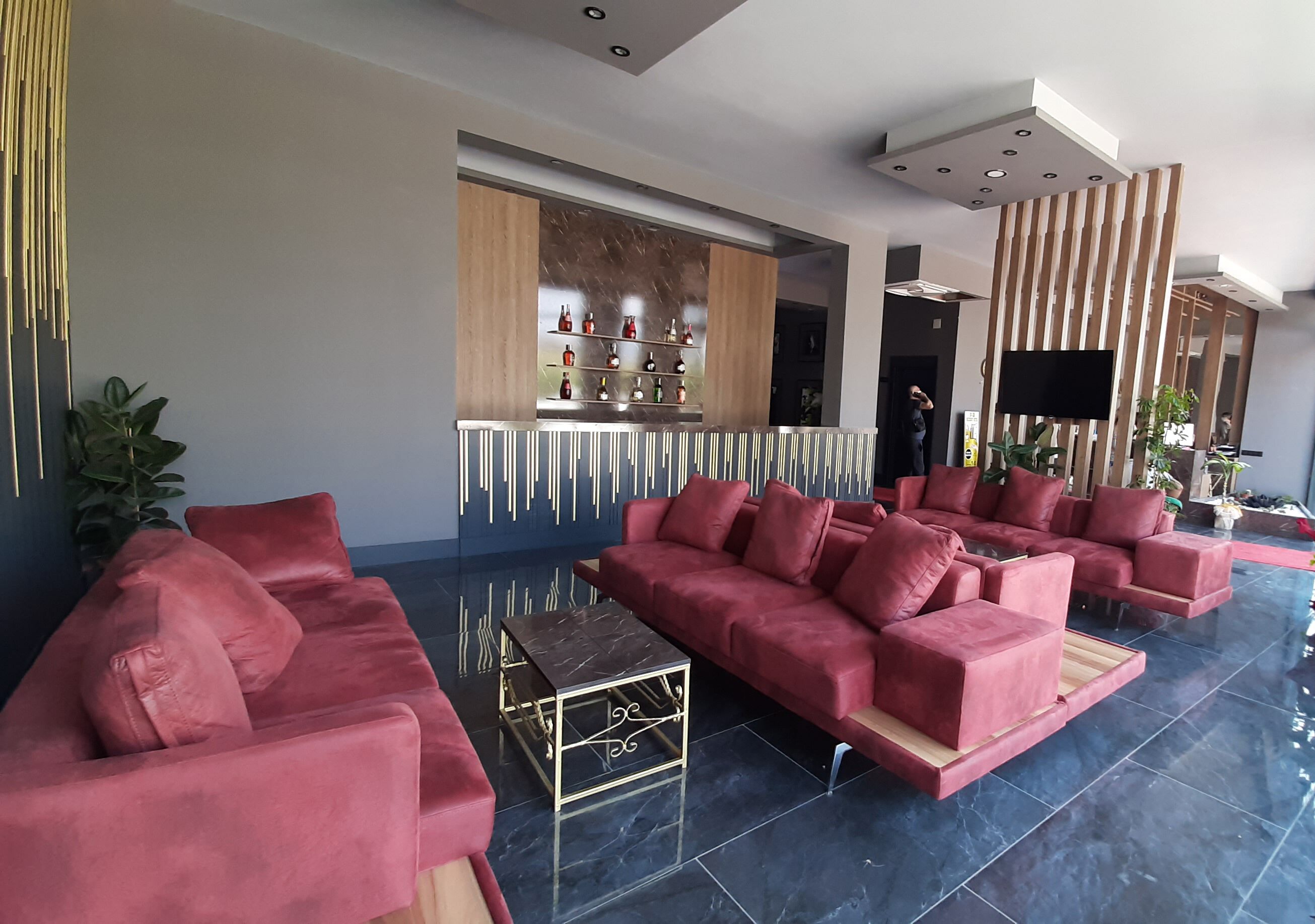 A modern lobby with a red sofa set, a bar area with shelves of bottles, and a flat-screen TV mounted on the wall.