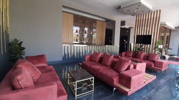 A modern lobby with a red sofa set, a bar area with shelves of bottles, and a flat-screen TV mounted on the wall.