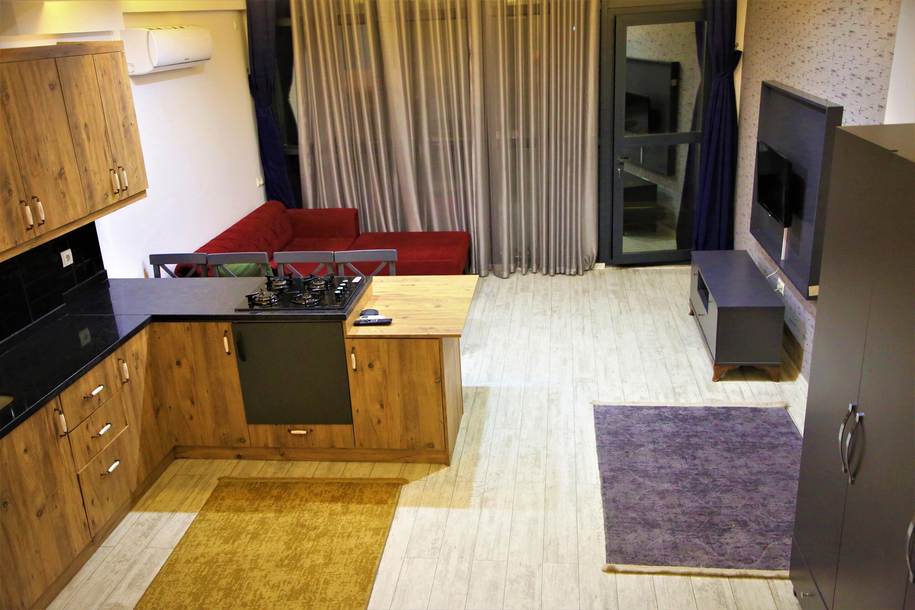 Una cocina compacta con armarios de madera, estufa integrada y un pequeño comedor con sofá rojo.