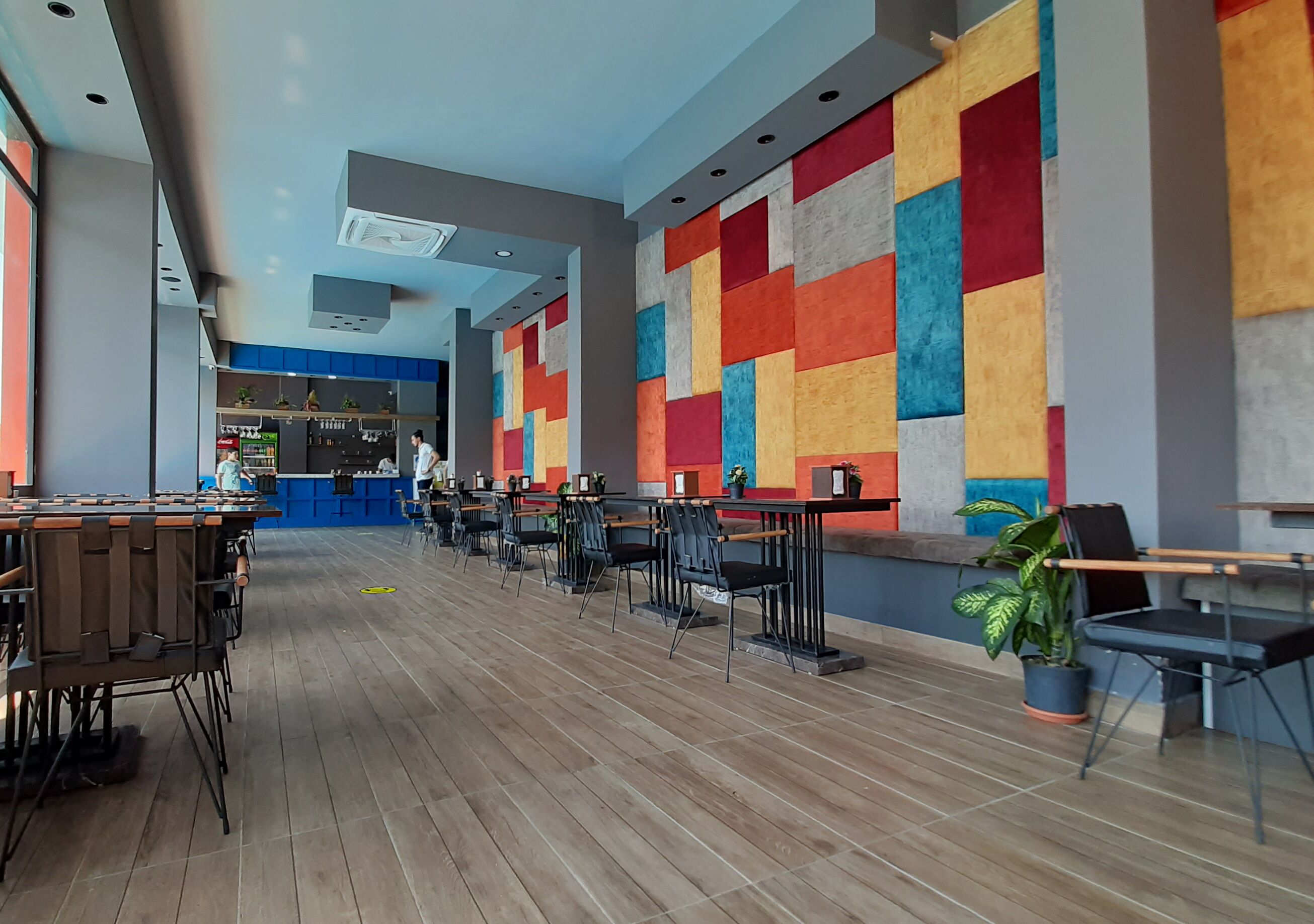 Un restaurante moderno con suelo de madera, sillas negras y un diseño de pared colorido.