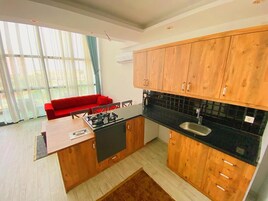 A modern kitchen with wooden cabinets, a black countertop, and a red sofa in the adjacent living area.