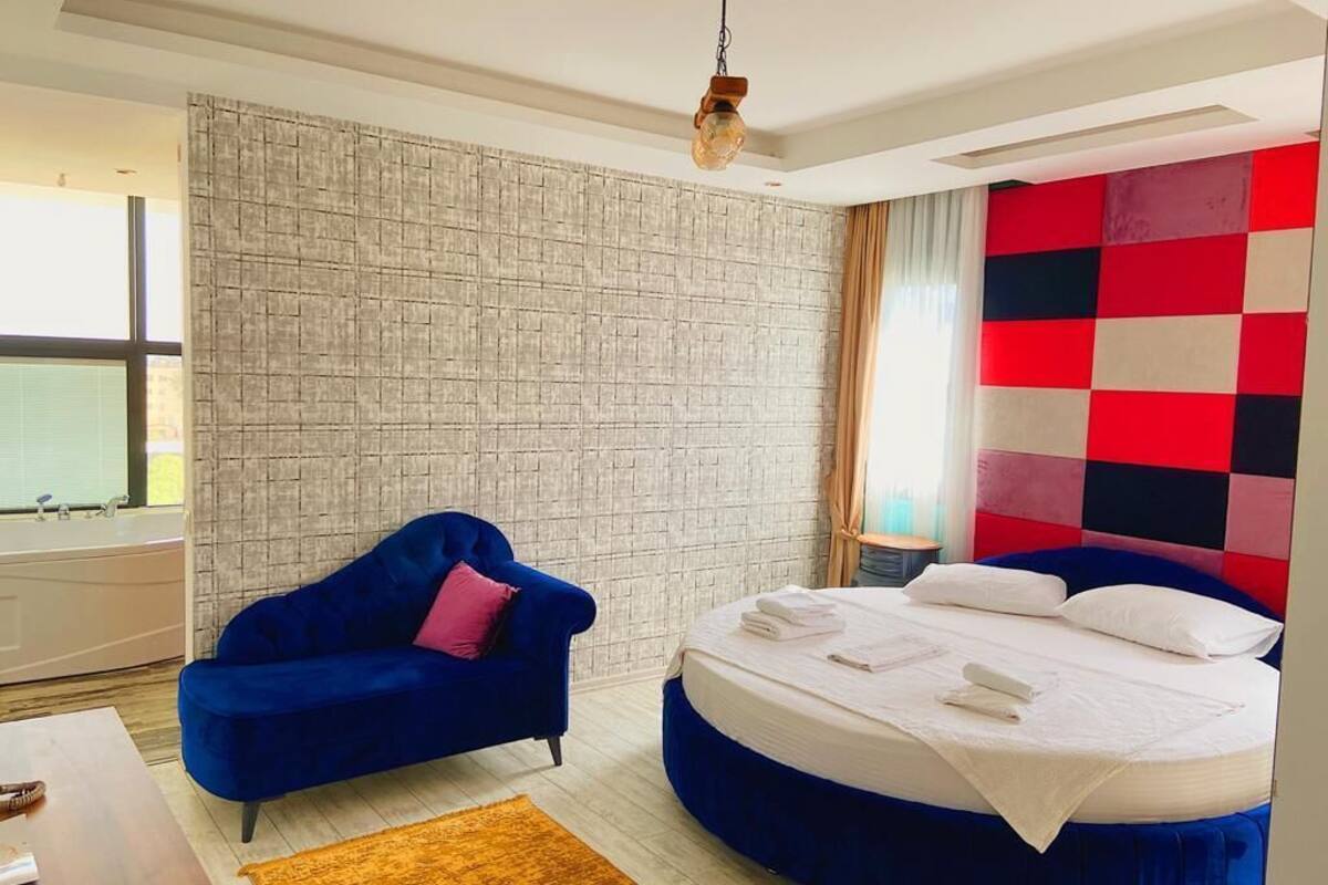 Quarto moderno com cama redonda, sofá azul, parede texturizada e parede quadriculada colorida.