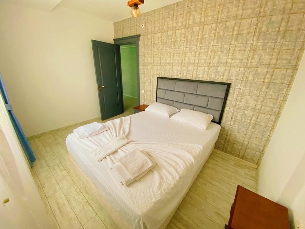 A neatly made bed with pillows and a blanket in a room with a textured wall and a wooden floor.