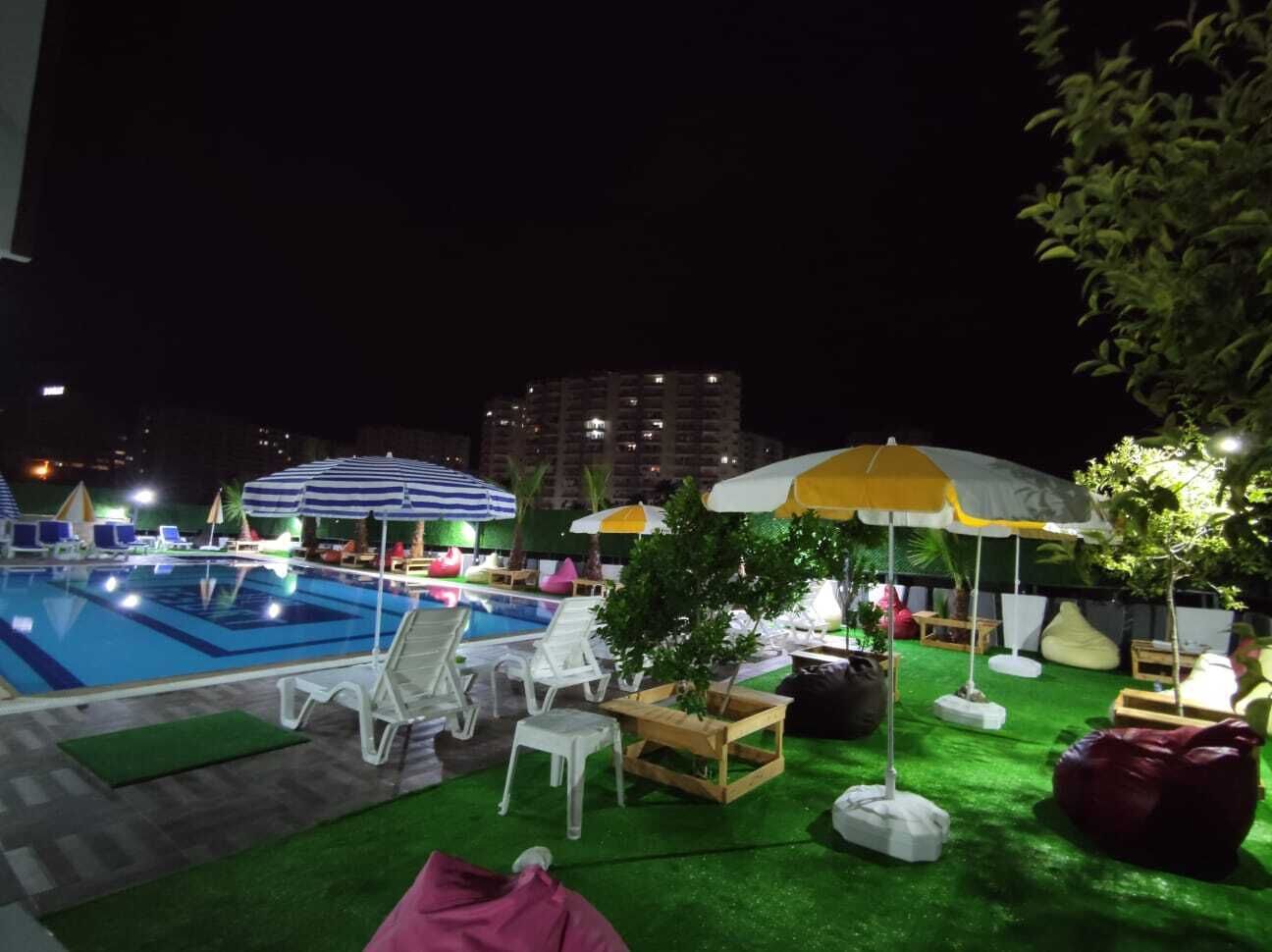 A nighttime outdoor pool area with lounge chairs, umbrellas, and artificial grass.
