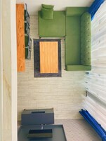 Una habitación con un sofá verde, un aparador de madera, una mesita pequeña y un ventanal con cortinas traslúcidas.