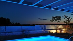 A rectangular swimming pool with a blue-lit edge, surrounded by a low wall and a fence.