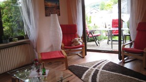 Una sala de estar con una mesa de centro de vidrio, sillas rojas, un sofá y vistas al patio exterior.