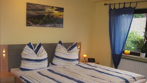 Un dormitorio con cama, ropa de cama a rayas, una mesita de noche, una lámpara, un cuadro en la pared y una ventana con cortinas.