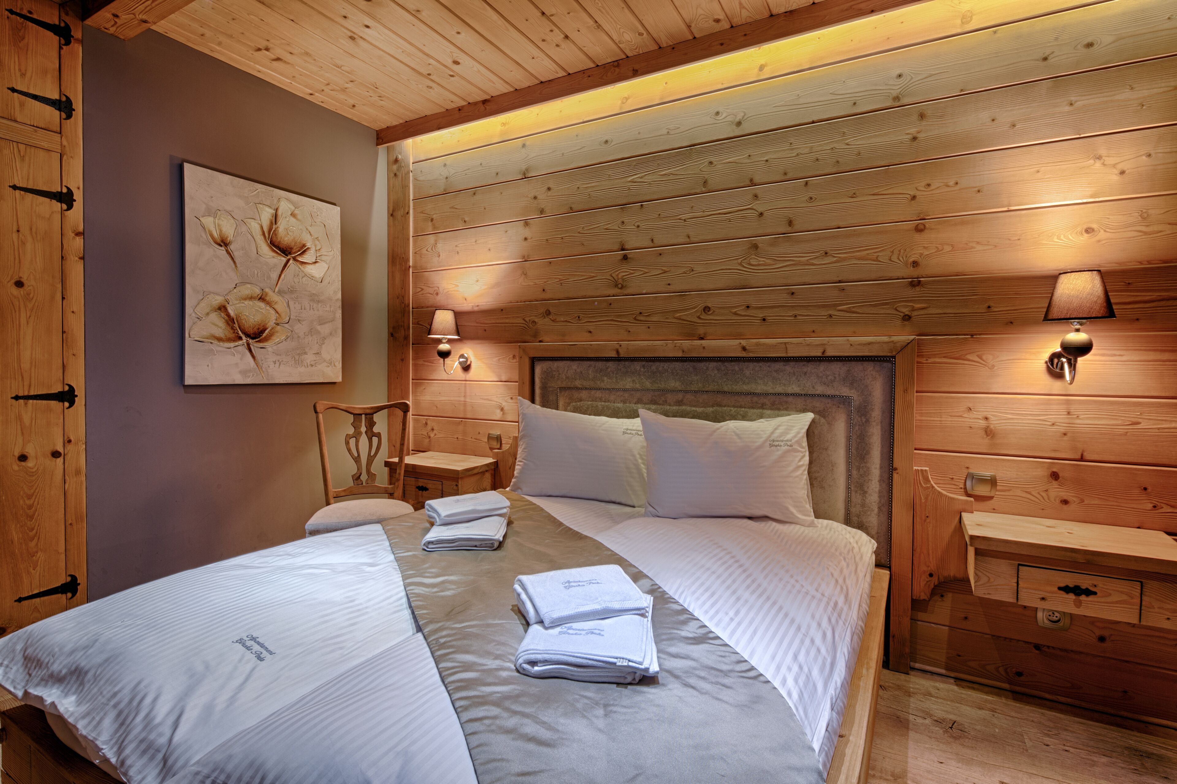 A wooden-paneled bedroom with a large bed, two bedside tables, and wall-mounted lamps.
