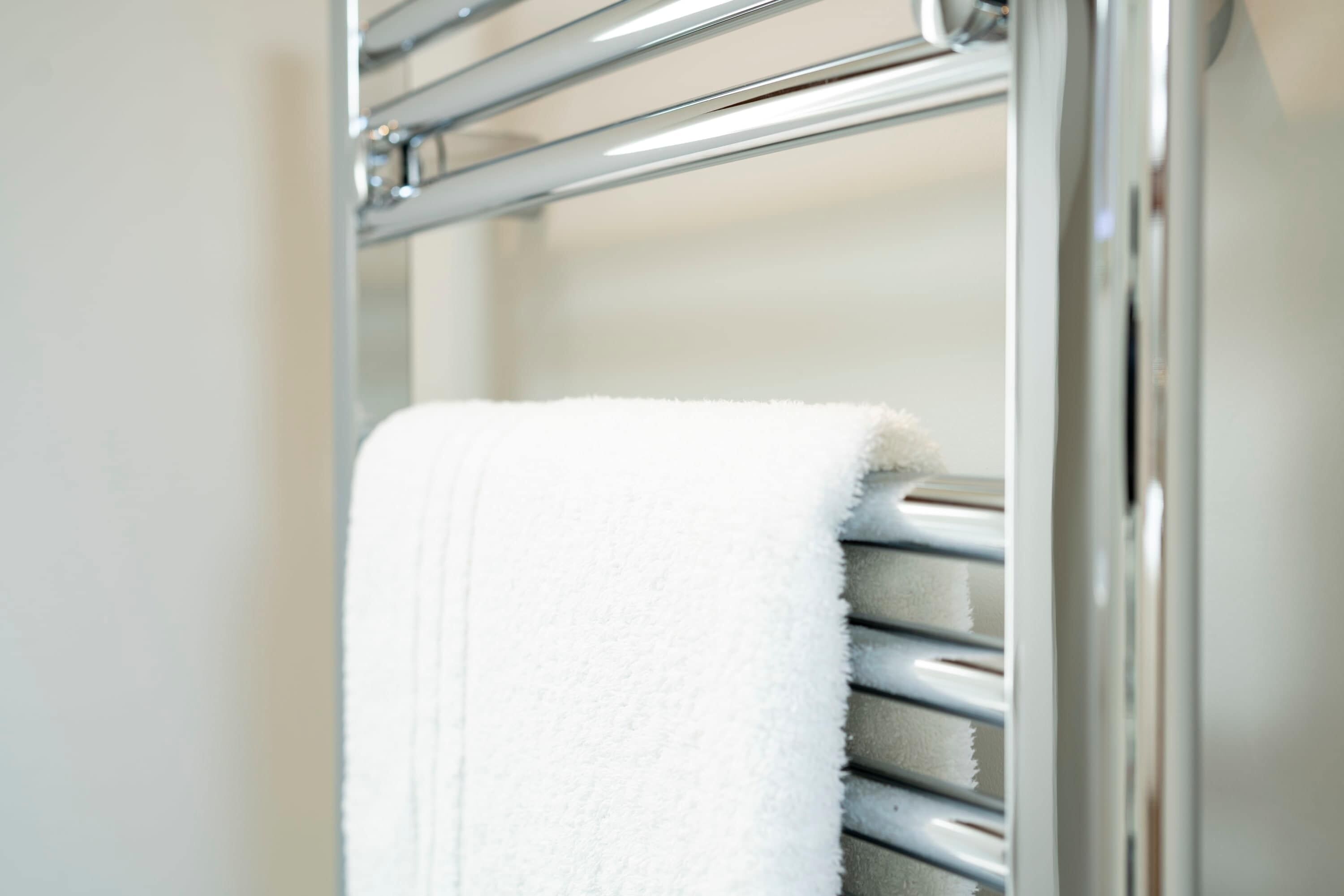 A white towel hanging on a chrome towel rack in a bathroom.