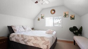 A bedroom with a bed, a window, a bench, and wall art.